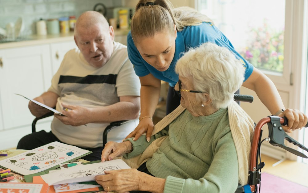 Caregiver helping two elderly residents with a colouring activity